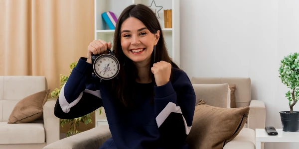 Smiling woman in black dress holding a small watch in her hand.