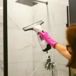 A woman cleaning a shower glass