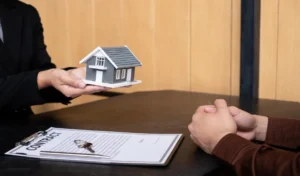 Midsection of person holding small house and contract with keys on table