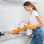 Young woman washing washbasin in protective gloves